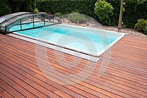 Outdoor swimming pool with cover enclosure and teak wood deck, exotic teakwood flooring stripes around blue water pool photo