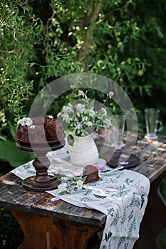 Outdoor table setting. Chocolate cake on a high wooden stand