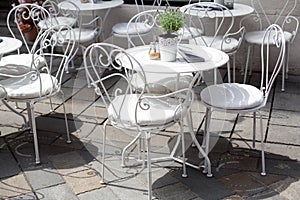 Outdoor terrace of cafe with beautiful white wrought iron chairs and table in sunny summer day. photo