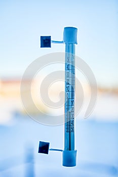 An outdoor thermometer is mounted on window glass using adhesive tape, scale shows 20 degrees Celsius below zero.