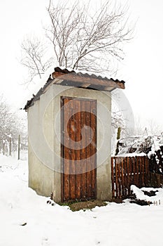 Outdoor toilet concrete building with wooden door in a village in Eastern Europe during snowfall in the winter