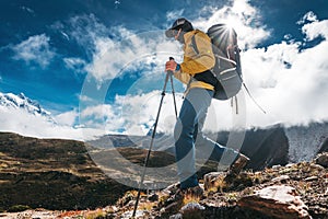 Outdoor tourist traveling along high altitude mountains wearing yellow jacket and professional backpack. Young solo hiker walk