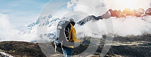 Outdoor tourist traveling along high altitude mountains wearing yellow jacket and professional backpack. Young solo hiker walk