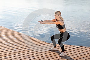 Outdoor Training. Smiling middle aged woman making squats exercise on the pier,