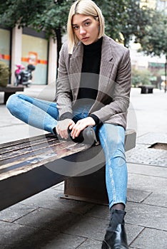 Outdoor urban female portrait. Fashion model. Young woman posing in Milan streets. Beautiful caucasian girl with blond hair sits