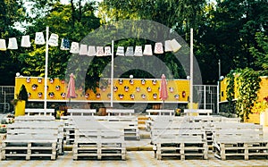 Outdoor venue. White benches on a background of a yellow wall with birdhouses and umbrellas