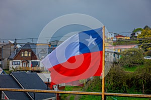 Outdoor view of Chilean flag waving with beautiful and colorful houses on stilts palafitos behind in the horizont in