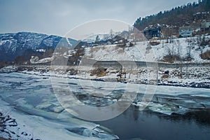 Outdoor view of frozen river with some wooden houses at one side of the road at Gol Mountain Are