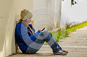 Outdoor view of homeless woman begging on the street in cold autumn weather sitting on the floor at sidewalk with a