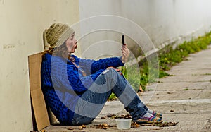 Outdoor view of homeless woman begging on the street in cold autumn weather sitting on the floor at sidewalk with a