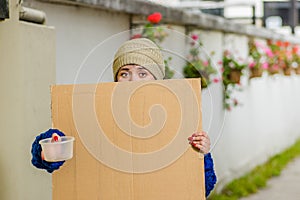 Outdoor view of homeless woman holding up blank cardboard sign