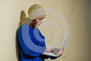 Outdoor view of homeless woman on the street in cold autumn weather holding a computer, at sidewalk
