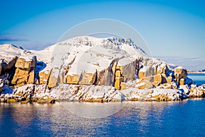 Outdoor view of snowy rock mountain covered during winter in the Arctic Circle, in a gorgeous blue sky and blue water