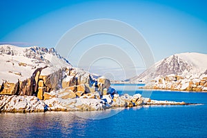 Outdoor view of snowy rock mountain covered during winter in the Arctic Circle, in a gorgeous blue sky and blue water