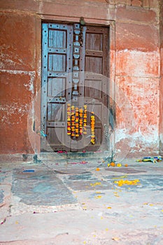 Outdoor view of a wooden door with some yellow flowers hanging, in a old house, in Agra city near of Taj Mahal in India