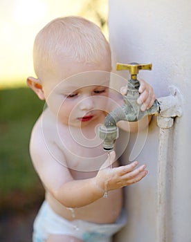 Outdoor, water and a baby playing at a tap in a summer garden at home. Little kid, childhood growth and adorable infant