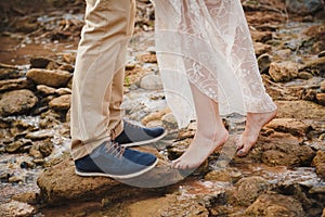 Outdoor wedding ceremony, close up of young woman feet standing barefoot on stones in front of mans feet wearing dark blue shoes