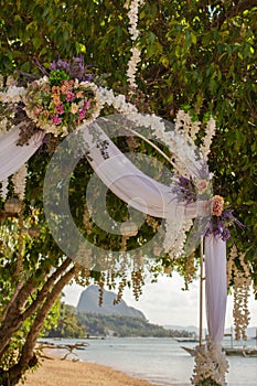 Outdoor wedding ceremony on tropical beach. Wedding decoration under palm trees. Exotic wedding. Wedding floral arch with bouquet.