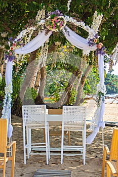 Outdoor wedding ceremony on tropical beach. Wedding decoration under palm trees. Exotic wedding. Wedding floral arch and chairs.