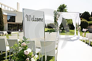 Outdoor wedding ceremony. Welcome plate decorated with fresh flowers on wedding chuppa background