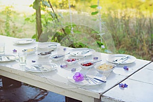 Outdoor white vintage table set for breakfast. Nicely decorated with fresh violet flowers and delicious food