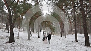 Outdoor winter forest shot of young wedding couple walking and having fun holding hands in snow weather pine forest