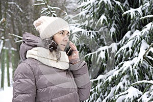 Outdoor winter portrait. Beautiful woman 45 years old talking on a cell phone in a snowy winter park