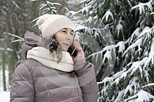 Outdoor winter portrait. Beautiful woman 45 years old talking on a cell phone in a snowy winter park