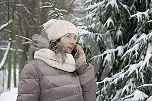Outdoor winter portrait. Beautiful woman 45 years old talking on a cell phone in a snowy winter park