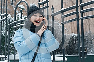 Outdoor winter portrait of mature woman with mobile phone on snowy city street, woman smiling talking