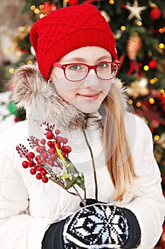 Outdoor winter young blonde teen girl portrait. At background blurred christmas tree.