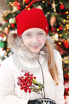 Outdoor winter young blonde teen girl portrait. At background blurred christmas tree.