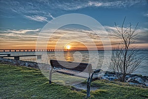 Outdoor wooden bench facing the Oresund Strait with a sunset over the massive Oresund Bridge Oresundsbron in the Baltic Sea