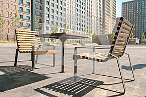 Outdoor wooden furniture on an iron frame in the square in front of a multi-storey residential complex