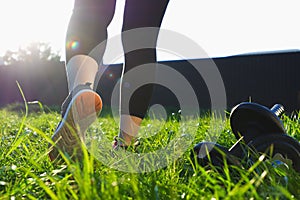 Outdoor workout. A woman walks on the grass in the backlight of the setting sun. Back view of legs in running shoes close-up.