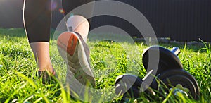 Outdoor workout. A woman walks on the grass in the backlight of the setting sun. Back view of legs in running shoes close-up.