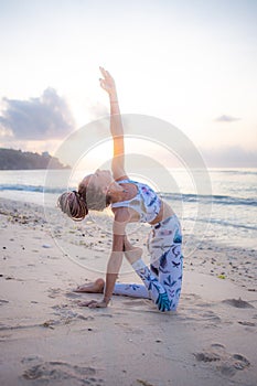 Outdoor yoga on the beach. Young woman practicing variation of Ushtrasana  Camel Pose  kneeling back bending asana. Flexible spine