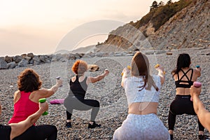 Outdoor yoga and fitness. Back view of group adult fit women are training with dumbbells on pebble beach. Concept of