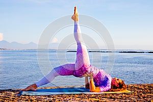 Outdoor yoga practice. Attractive woman practicing variation of Setu Bandhasana, Shoulder supported bridge pose with one leg up.