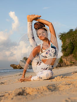 Outdoor yoga practice near the ocean. Attractive woman practicing Eka Pada Sirsasana, Foot-behind-the-Head Pose. Flexible healthy