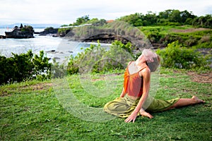 Outdoor yoga practice. Young woman practicing Ardha Kapotasana, Half Pigeon Pose. Chest opener improving breathing. Tanah Lot