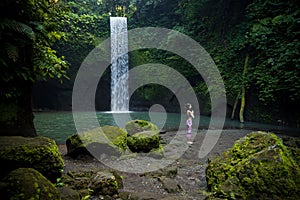 Outdoor yoga practice. Young woman standing near waterfall. Hands in namaste mudra, closed eyes. Preparing for Sun salutation