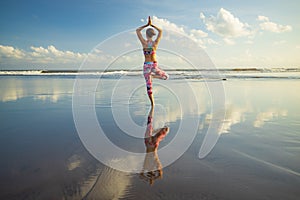 Outdoor yoga. Vrikshasana asana. Slim woman practicing tree pose on the beach. Water reflection. Perfect balance. Yoga retreat.