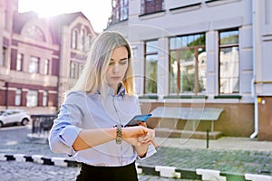 Outdoor young business woman with smartphone looking at wrist watch