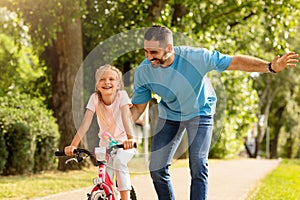 Outdoors activities. Happy father teaching his daughter to ride a bike in the park, enjoying time together on weekend