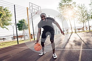 Outdoors Activity. African man playing basketball on court dribbling smiling excited