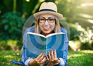 The outdoors is the best place to read. Portrait of an attractive young woman reading a book while lying outside on the