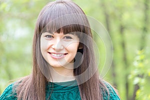 Outdoors closeup portrait of young beautiful woman brunette girl happy smiling & looking at camera on summer green background