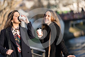 Outdoors fashion portrait of two young beautiful women friends drinking coffee