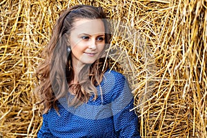 Outdoors fashion portrait of young woman in blue dress sitting near haystack